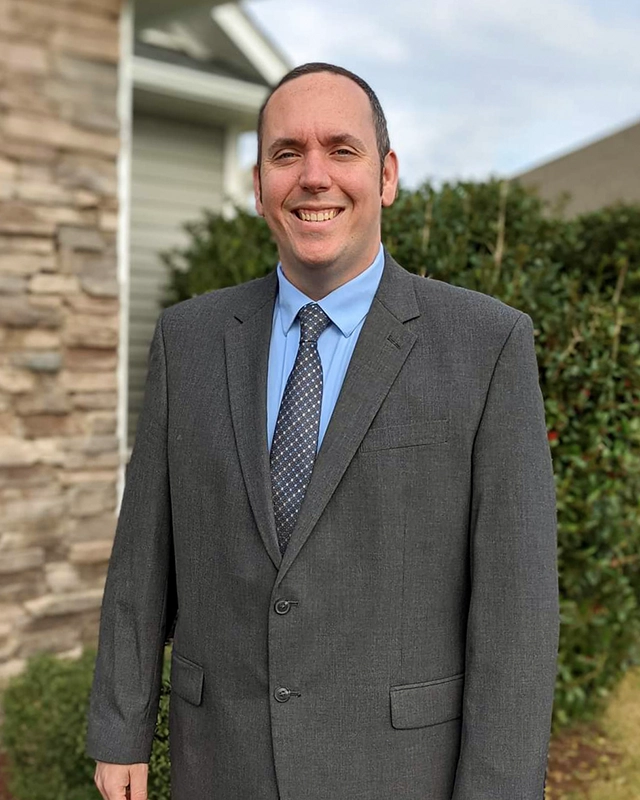 Chris Schulte smiling while standing outside in a suit and tie.